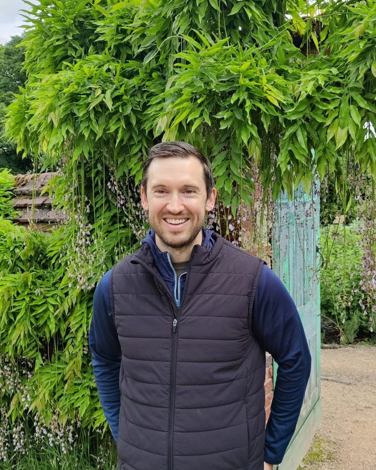Dr Daniel O'Rourke standing under wisteria beside a green garden door